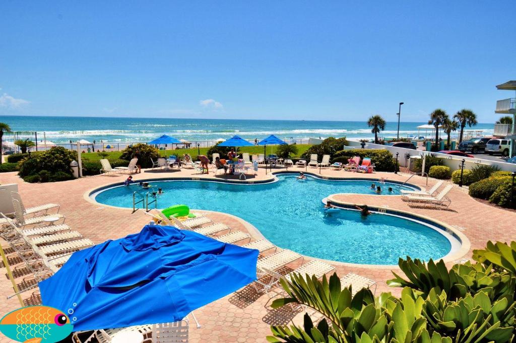 una piscina con sillas y sombrillas azules y el océano en "SHERWIN" Coastal Vibes Oceanfront Condominiums en Daytona Beach