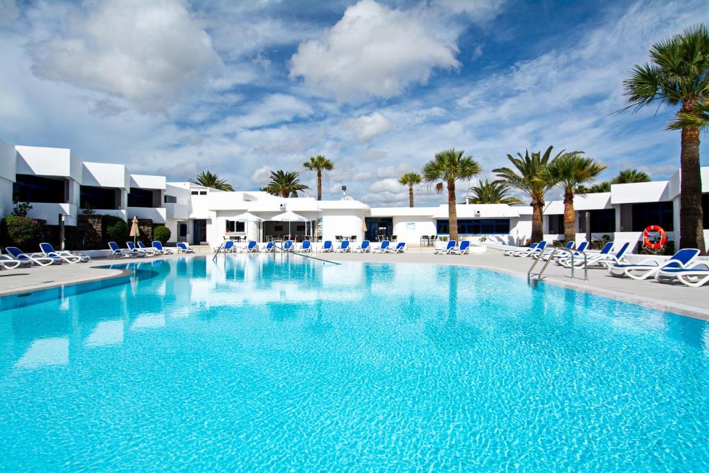 una gran piscina con sillas y palmeras en Apartamentos Panorama Adults Only, en Puerto del Carmen