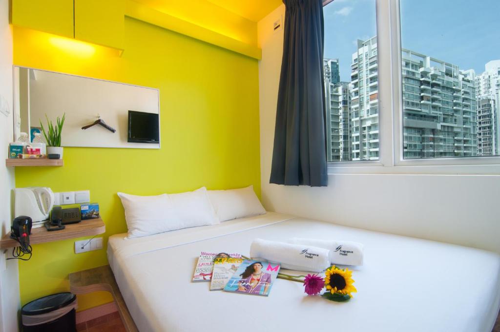 a bedroom with a bed with a yellow wall and a window at Fragrance Hotel - Classic in Singapore