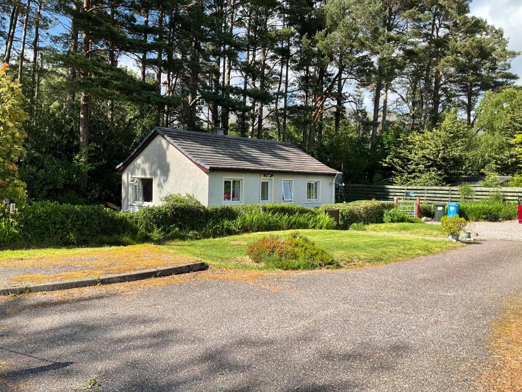 uma pequena casa branca na berma de uma estrada em The Pines Self-catering cottage,Wester Ross, Scotland em Kinlochewe