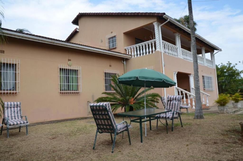 einen Tisch mit Stühlen und einen Regenschirm vor einem Haus in der Unterkunft Palm Tree Guest House in Manzini