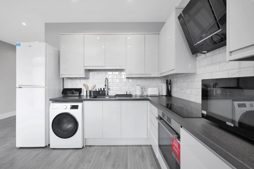 a kitchen with white cabinets and a washer and dryer at Your Cosy Stay Modern 1 Double Bedroom Flat Fully Furnished - 5 Mins walk to Stn in London
