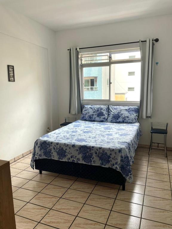 a bedroom with a bed with a blue comforter and a window at Quarto privativo in Balneário Camboriú