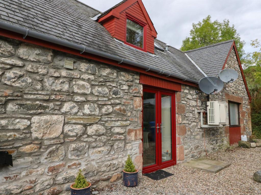 a stone cottage with red doors and a stone wall at Kerrowdown Mill in Inverness