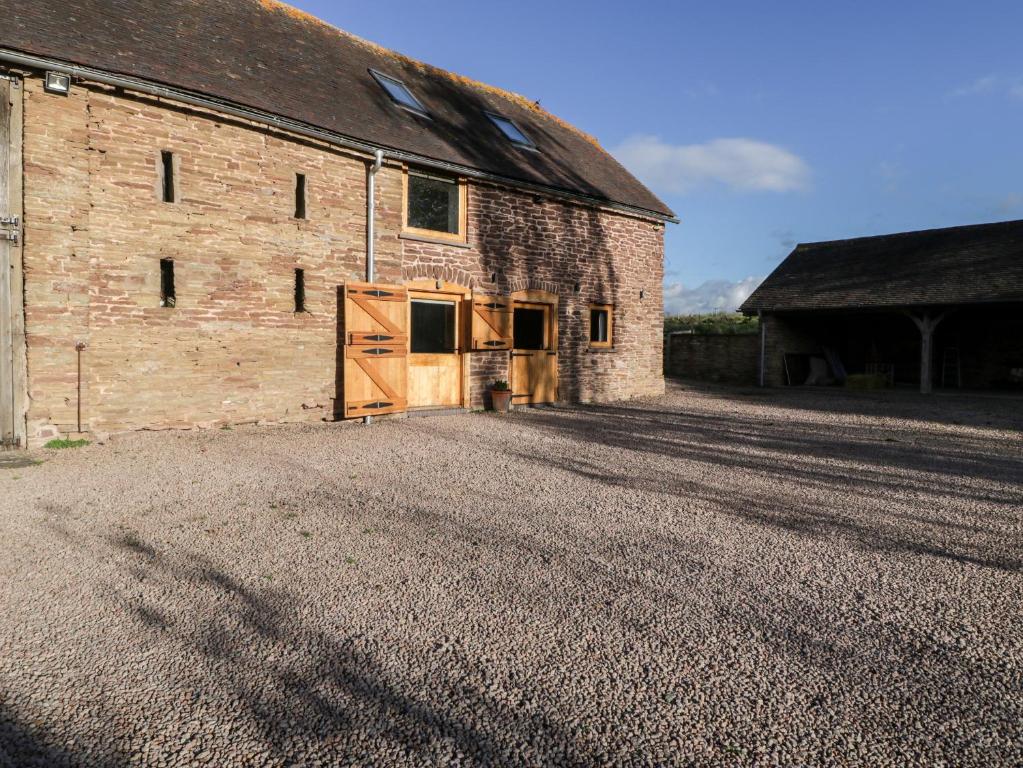 an old brick barn with a door on a gravel driveway at Barn Cottage in Leominster