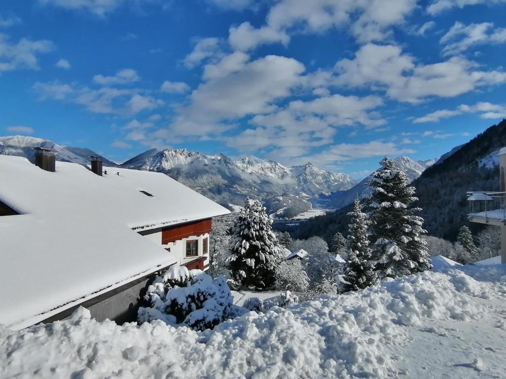 a house covered in snow with mountains in the background at Landhaus Berthold in Bürserberg
