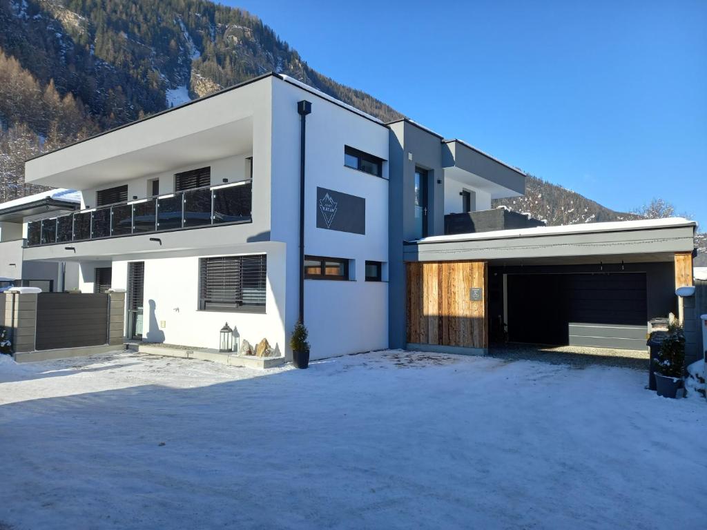 ein weißes Haus mit Garage und Bergen im Hintergrund in der Unterkunft Apart Katja in Längenfeld