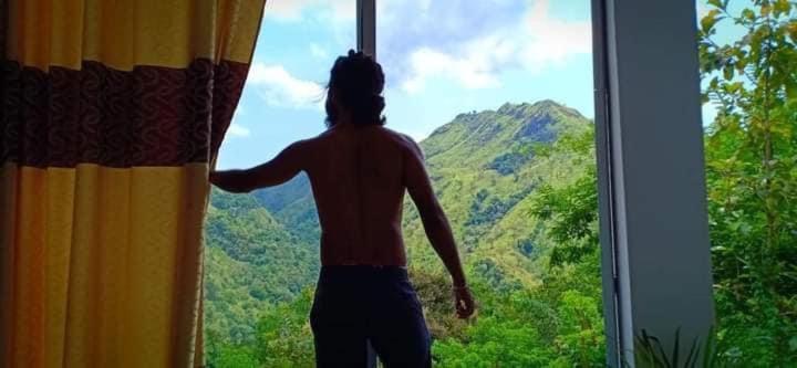Un uomo che guarda fuori da una finestra su una montagna di Paradise view hostel a Ella