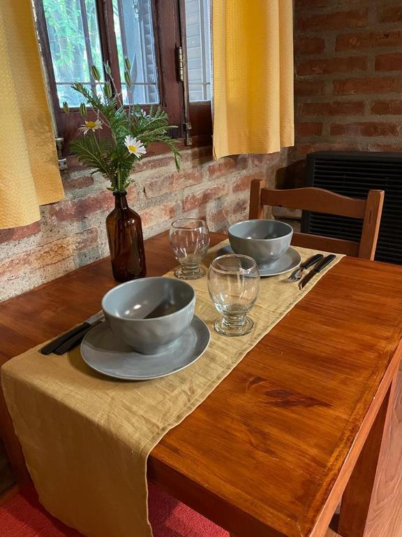 a wooden table with two bowls and glasses on it at Alojamiento ¨El Puente¨ en El Bolsón, para dos personas. in El Bolsón