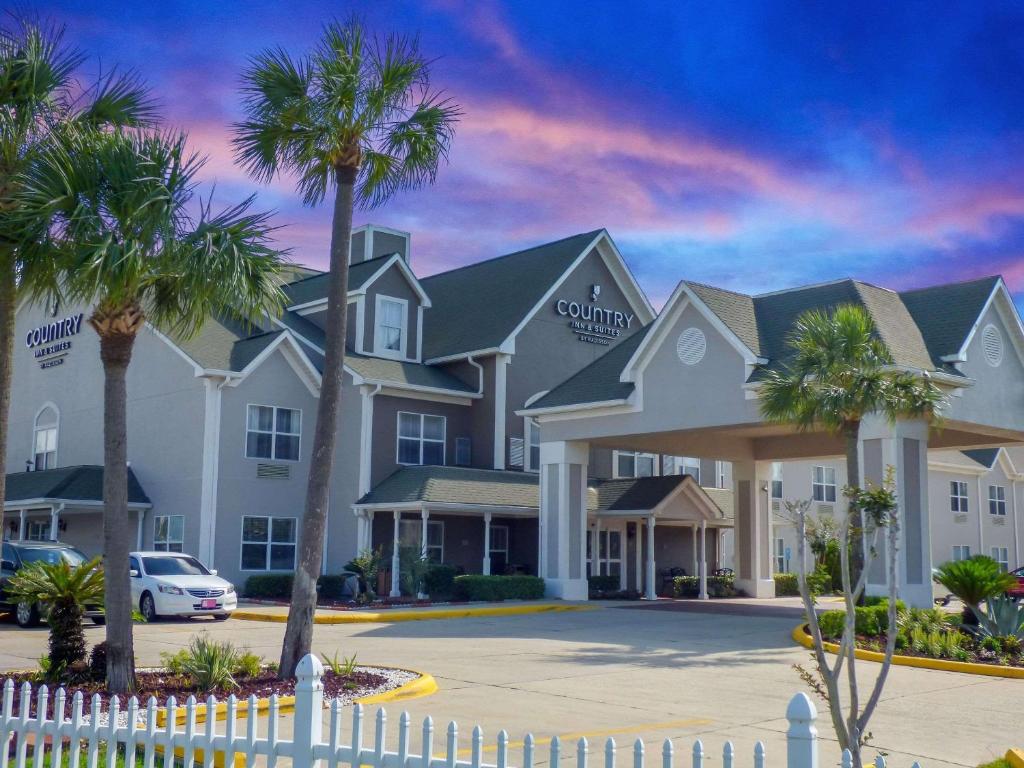 Country Inn & Suites by Radisson, Biloxi-Ocean Springs, MS في أوشن سبرينغز: مبنى كبير أمامه أشجار نخيل