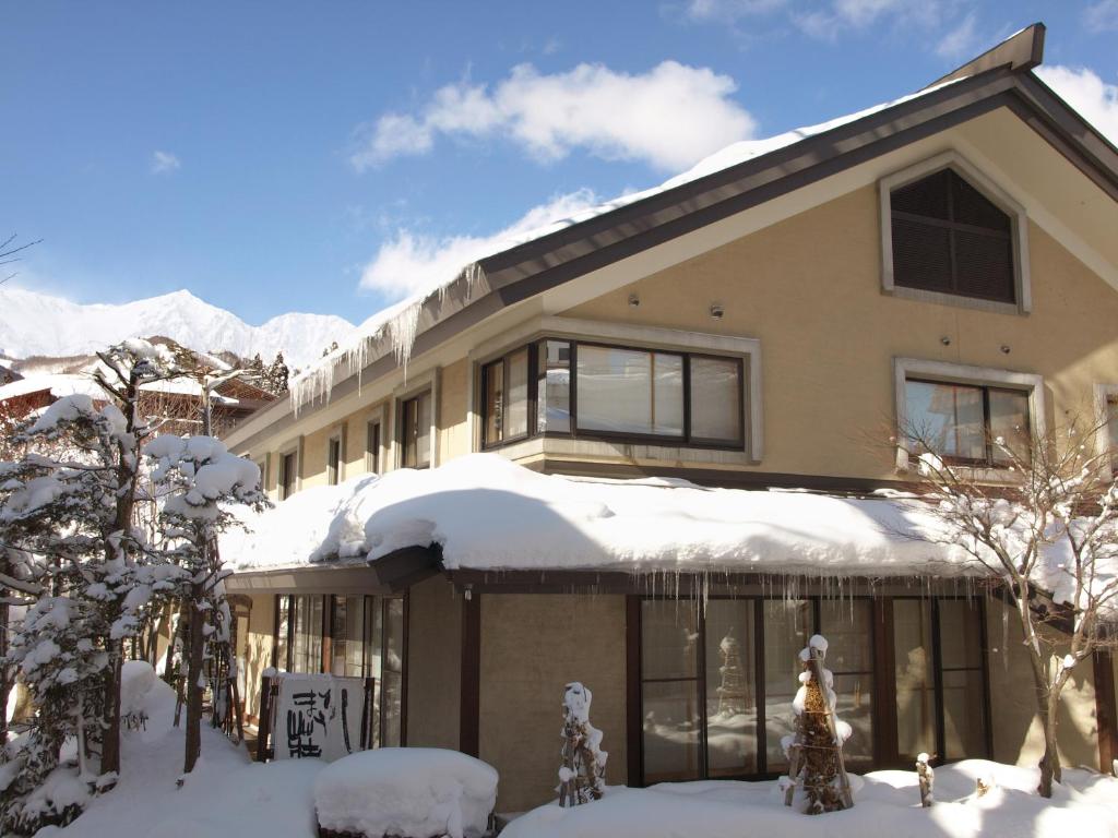 a house covered in snow with mountains in the background at Hakuba Onsen Ryokan Shirouma-so in Hakuba