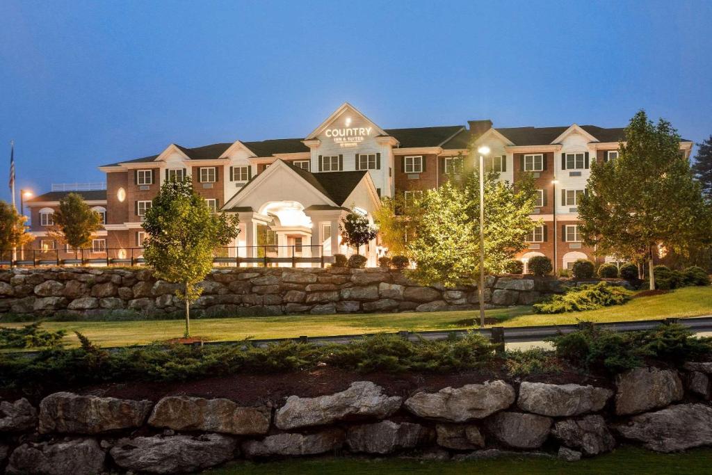 a large building with a stone wall in front of it at Country Inn & Suites by Radisson, Manchester Airport, NH in Bedford