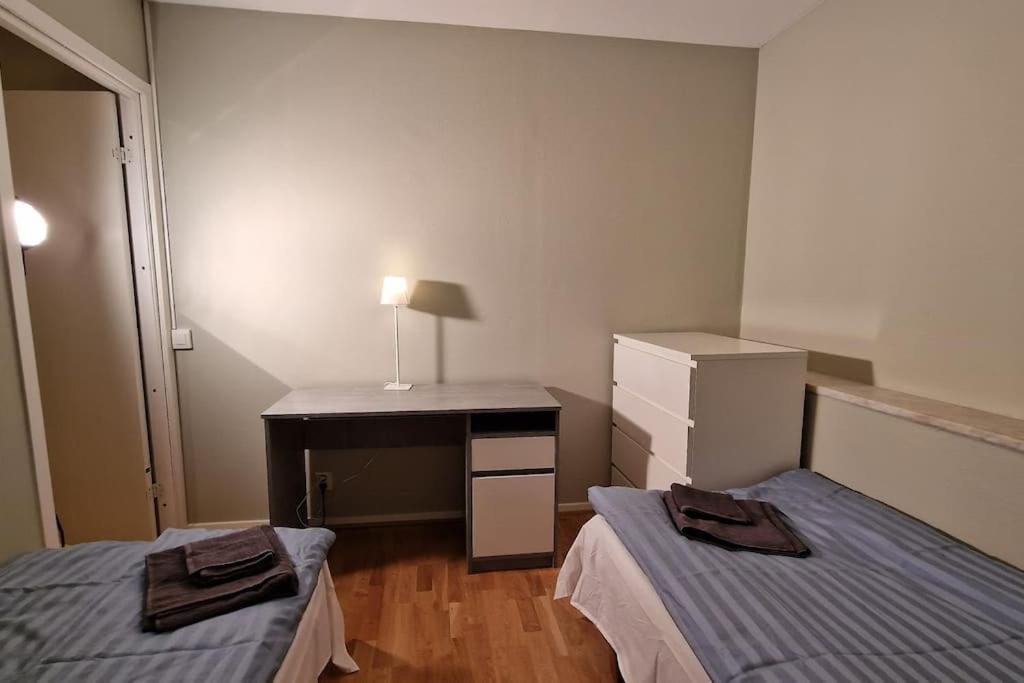 a room with two beds and a desk with a lamp at Mysigt Stadsoas: En Modern lägenhet med 2 sovrum in Gothenburg