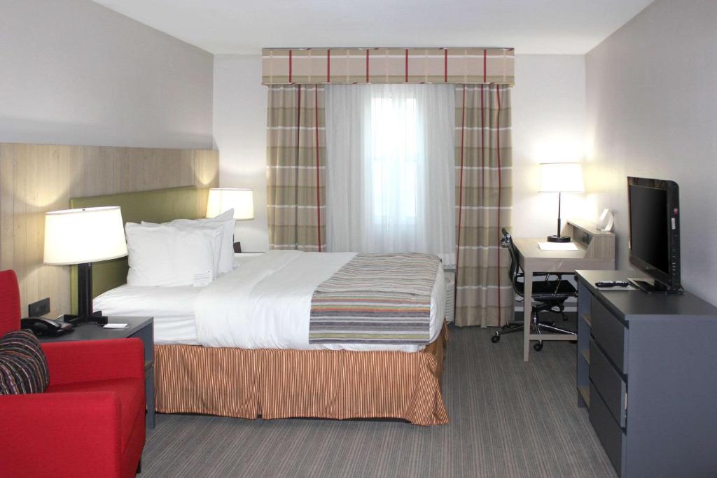 Country Inn & Suites by Radisson, Sparta, WI في Sparta: غرفة فندقية فيها سرير ومكتب وتلفزيون