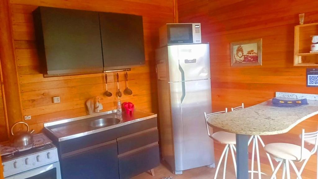 eine Küche mit einem Kühlschrank, einer Spüle und einem Tisch in der Unterkunft Cabanas dos Sonhos Barra de Ibiraquera in Imbituba