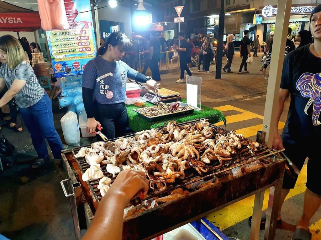 a woman is preparing food on a grill in a market at Stanton Gaya Hotel in Kota Kinabalu