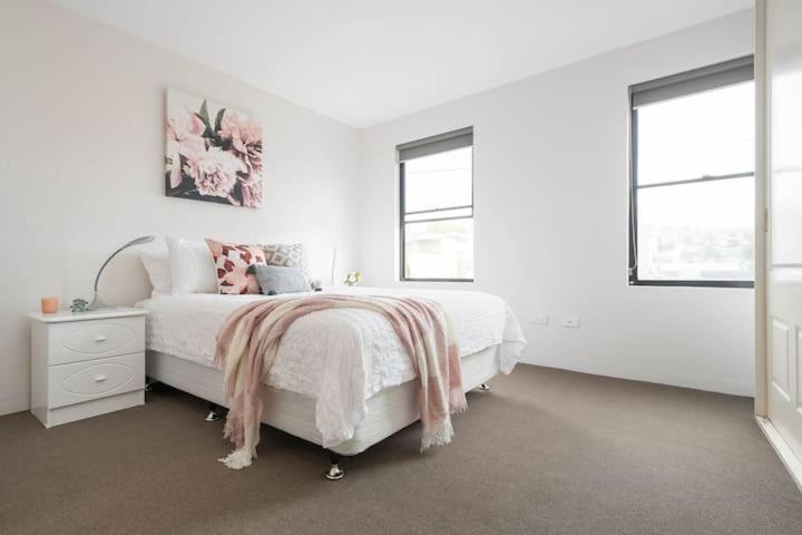 a white bedroom with a bed and two windows at CBD Apartment with WiFi & Parking in Launceston