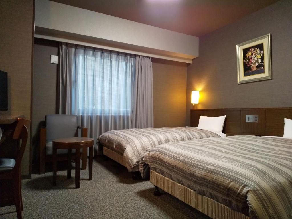 a hotel room with two beds and a window at Hotel Route-Inn Ashikaga Ekimae in Ashikaga