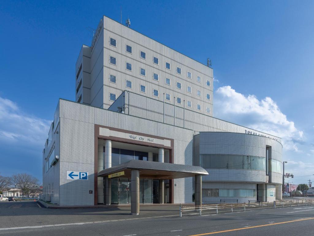 un gran edificio blanco con un estacionamiento delante de él en Tokai City Hotel en Tokai