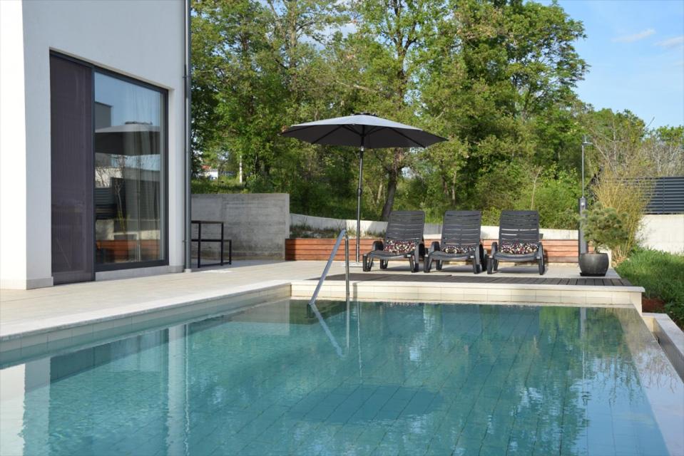 einen Pool mit zwei Stühlen und einem Sonnenschirm neben einem Haus in der Unterkunft Villa goISTRIA in Fuškulin