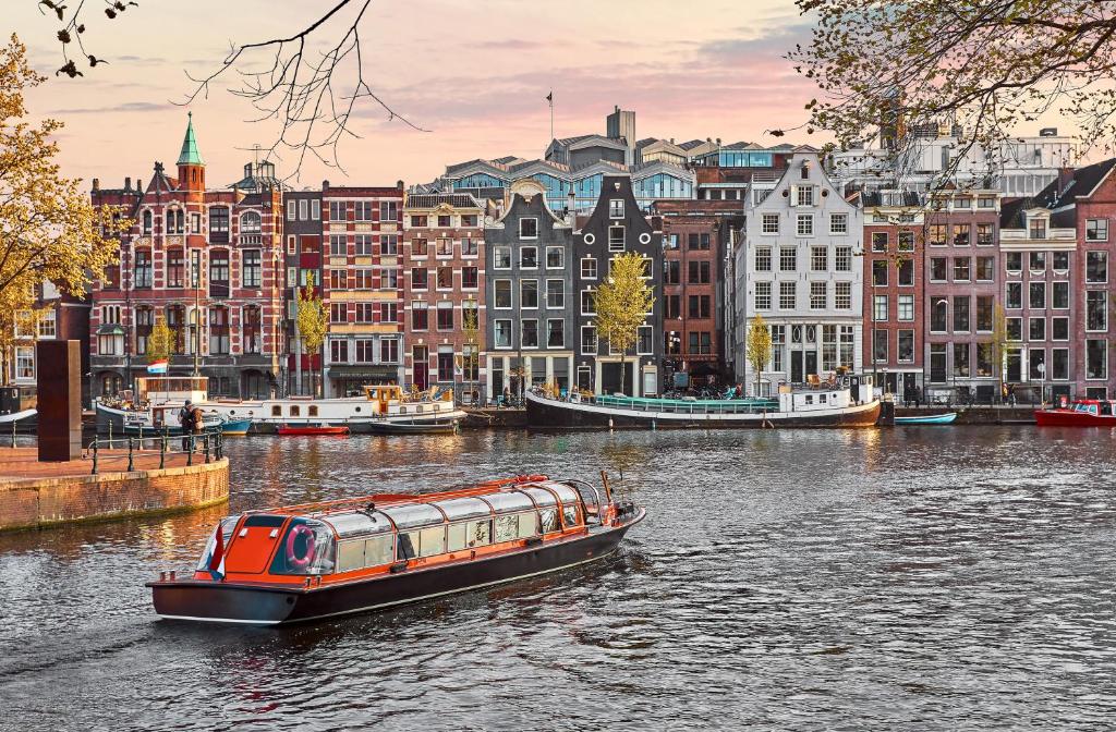 um barco em um rio em uma cidade com edifícios em Eden Hotel Amsterdam em Amesterdão