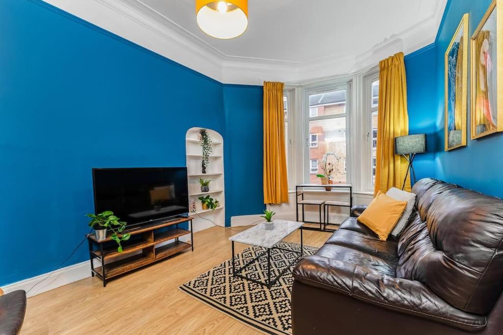 uma sala de estar com paredes azuis e um sofá de couro em Traditional 1-Bed Flat in Southside (Hampden/Shawlands) em Glasgow