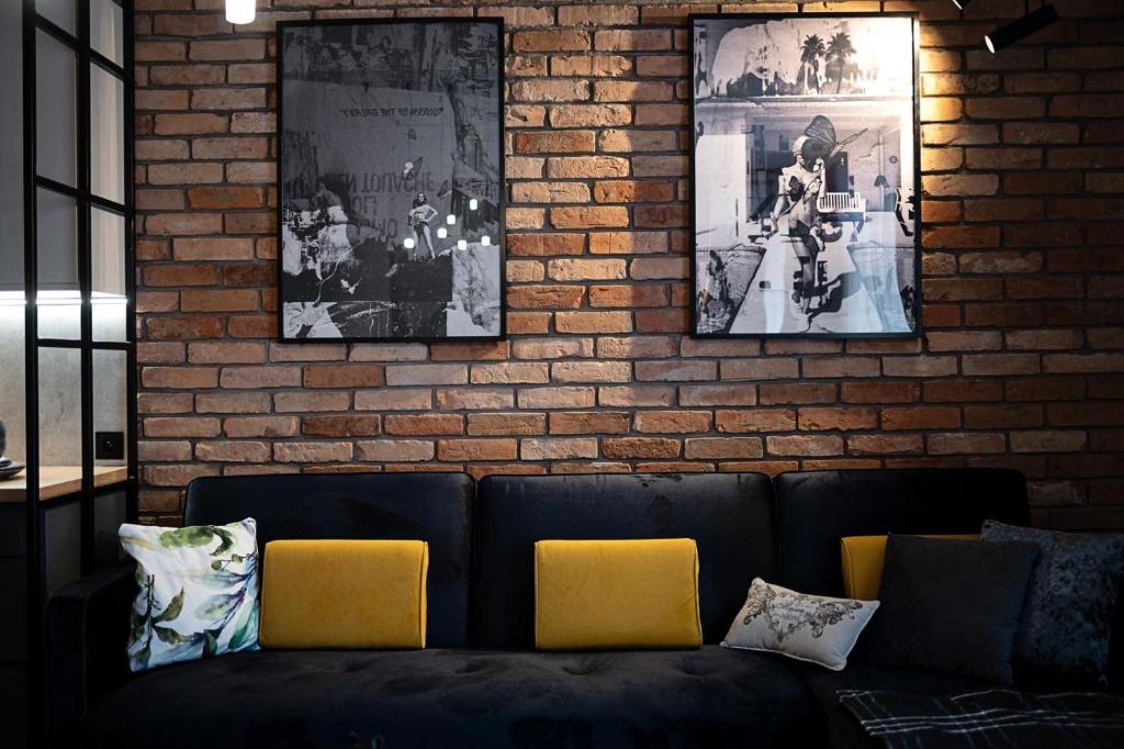 a black couch against a brick wall with pictures at Apartament pod gwiazdką in Tomaszów Mazowiecki