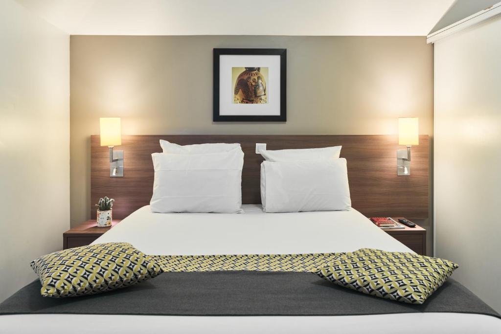 1 dormitorio con 1 cama grande con sábanas y almohadas blancas en Zenitude Hôtel Résidences Roissy Village en Roissy-en-France