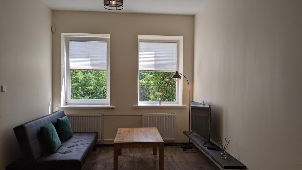 uma sala de estar com um sofá, uma mesa e 2 janelas em Guest House Kamara em Panevėžys