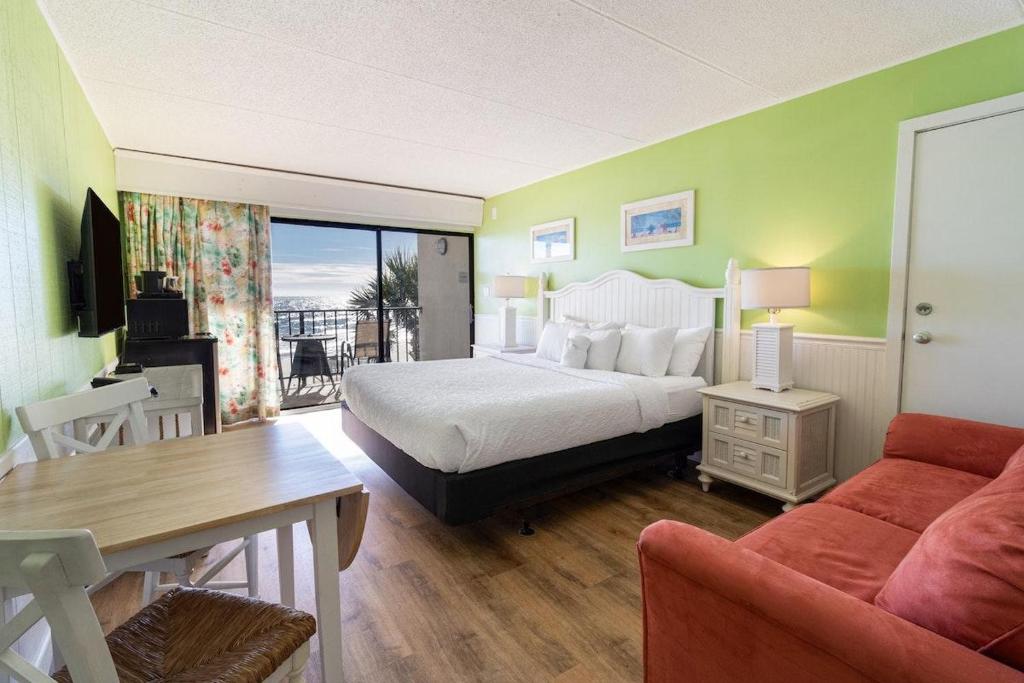 ein Schlafzimmer mit einem Bett, einem Tisch und einem Sofa in der Unterkunft Superb 3rd Floor Oceanfront King Room in Pawleys Island