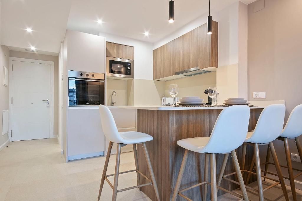 a kitchen with a bar with white stools at YOUR HOME- Apartment Camp Nou Baj in Hospitalet de Llobregat