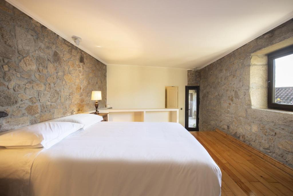 a bedroom with a white bed and a stone wall at Alma Peregrina - Casas de Campo in Junqueira