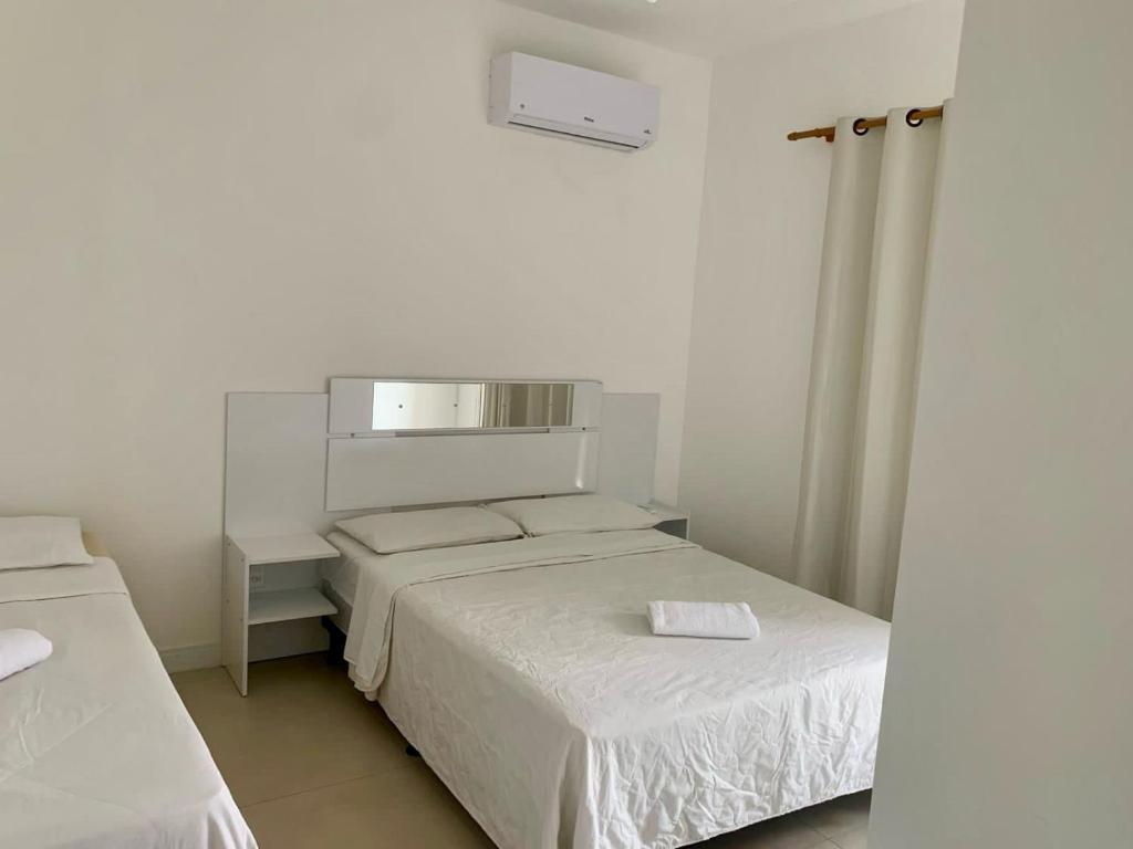 a white bedroom with two beds and a mirror at MDJ Suítes in Cabo Frio