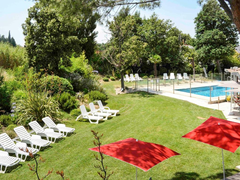 une pelouse avec des chaises et des parasols à côté d'une piscine dans l'établissement ibis Salon de Provence, à Salon-de-Provence