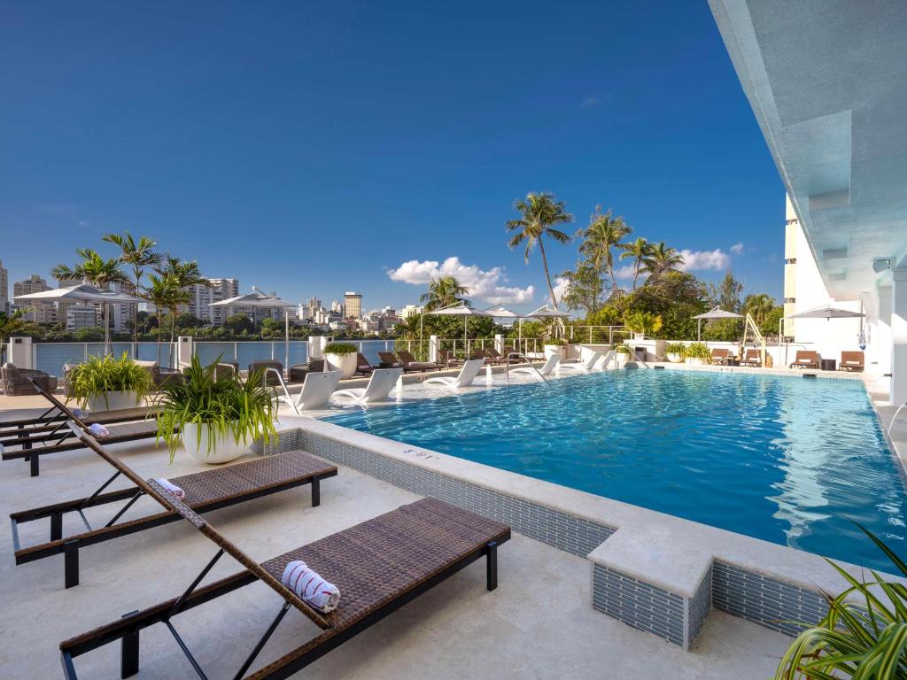 a swimming pool with chaises and chairs on a building at Hilton Garden Inn San Juan Condado in San Juan