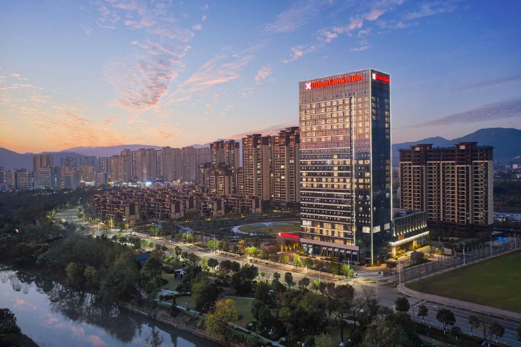a tall building with a red sign on it next to a river at Hilton Garden Inn Ganzhou Longnan in Longnan