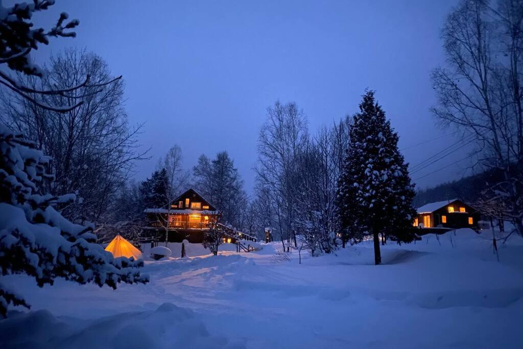 Una casa en la nieve por la noche con luces encendidas en Oasis biei, en Shibinai