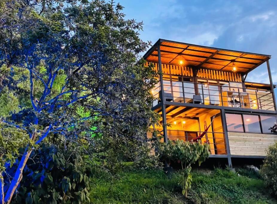 a house on a hill with trees in the foreground at Magma Home Cabaña Loft - Guatape Piscina-Jacuzzi in El Peñol