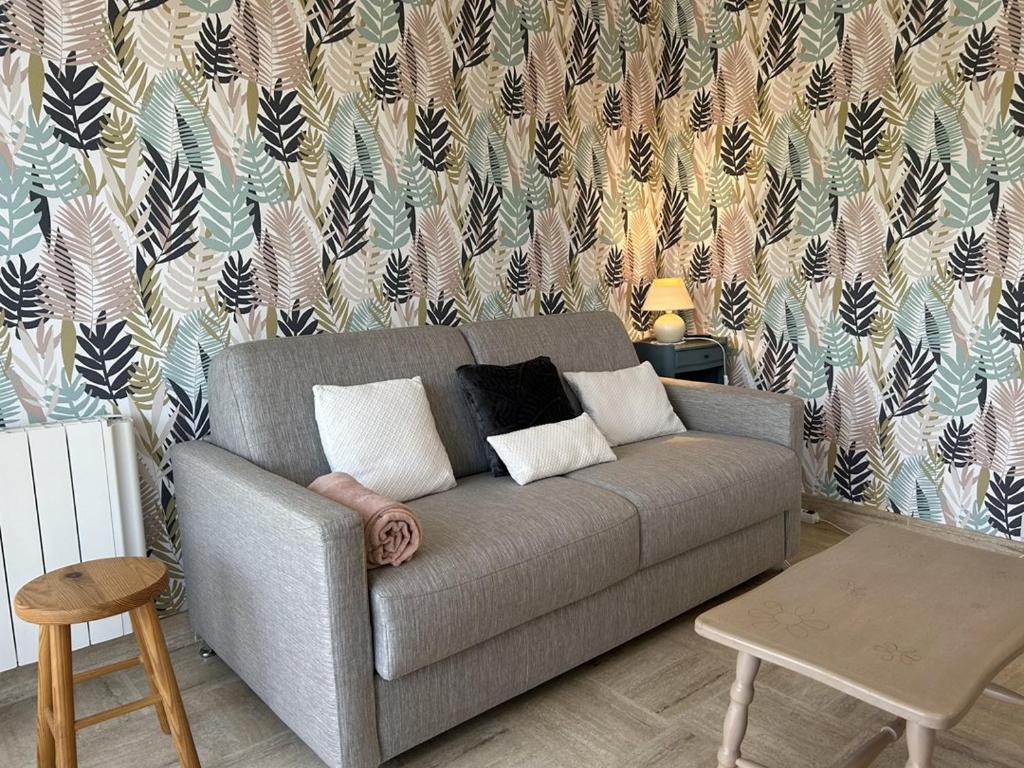 un salon avec un canapé gris et un papier peint dans l'établissement 541 - Studio en rez-de-jardin à quelques pas de la plage, à Erquy