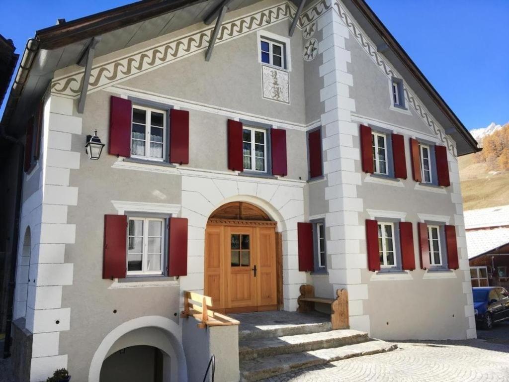una grande casa con porta in legno e persiane rosse di Zusammen mit Freiraum - ENGADIN HOLIDAYS a Guarda