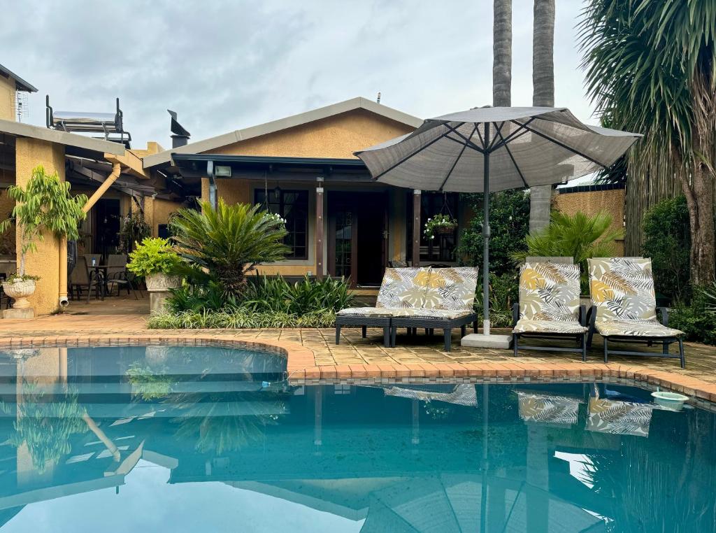 - une piscine avec 2 chaises et un parasol dans l'établissement Pin Oak Cottage, à Vryheid