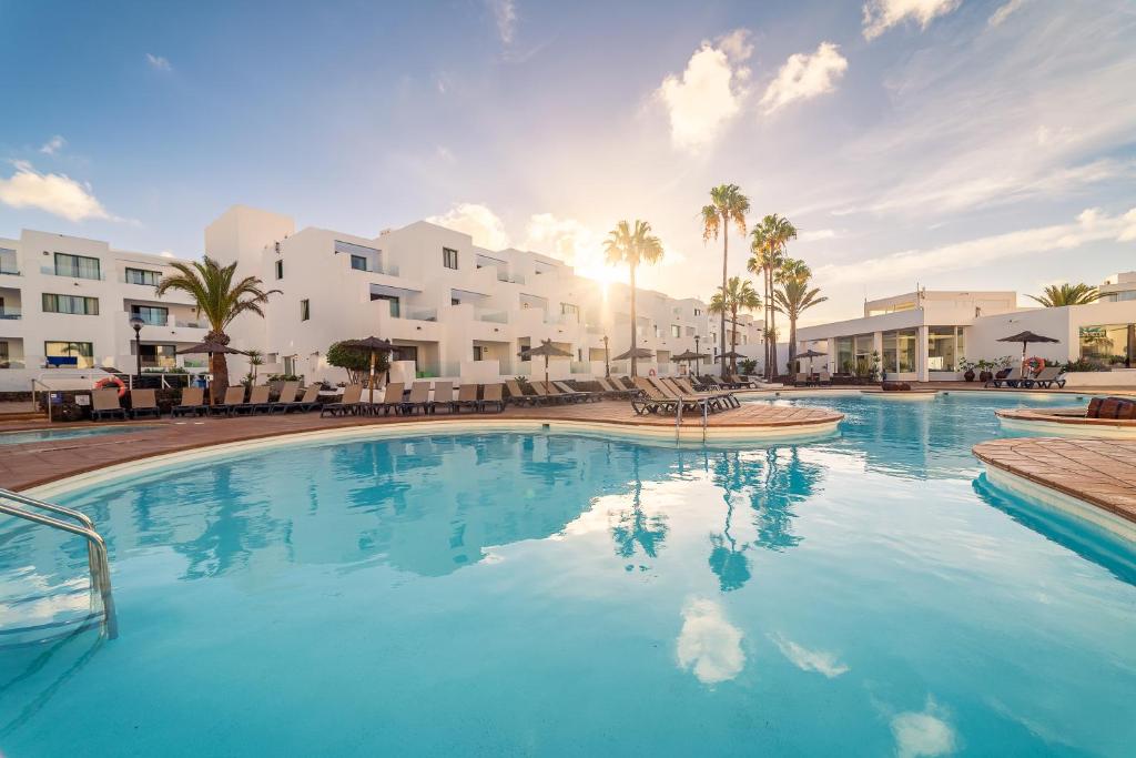 una piscina en un complejo con palmeras y edificios en Apartamentos Galeon Playa en Costa Teguise