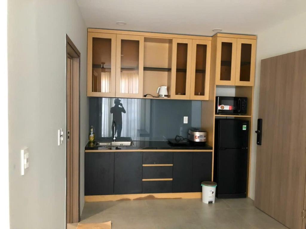 a kitchen with wooden cabinets and a black refrigerator at Novaworld Phan Thiết- 7Days mart in Phan Thiet