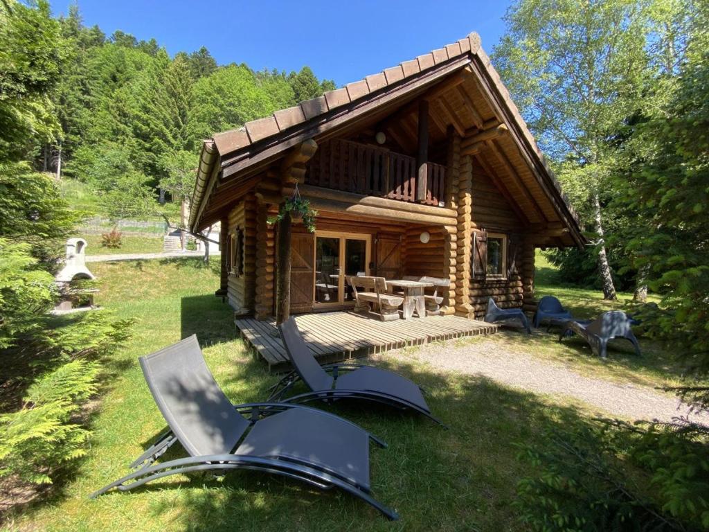 une cabane en rondins avec une terrasse et des chaises dans l'herbe dans l'établissement L'OURS NOIR Chalet en rondins, à La Bresse