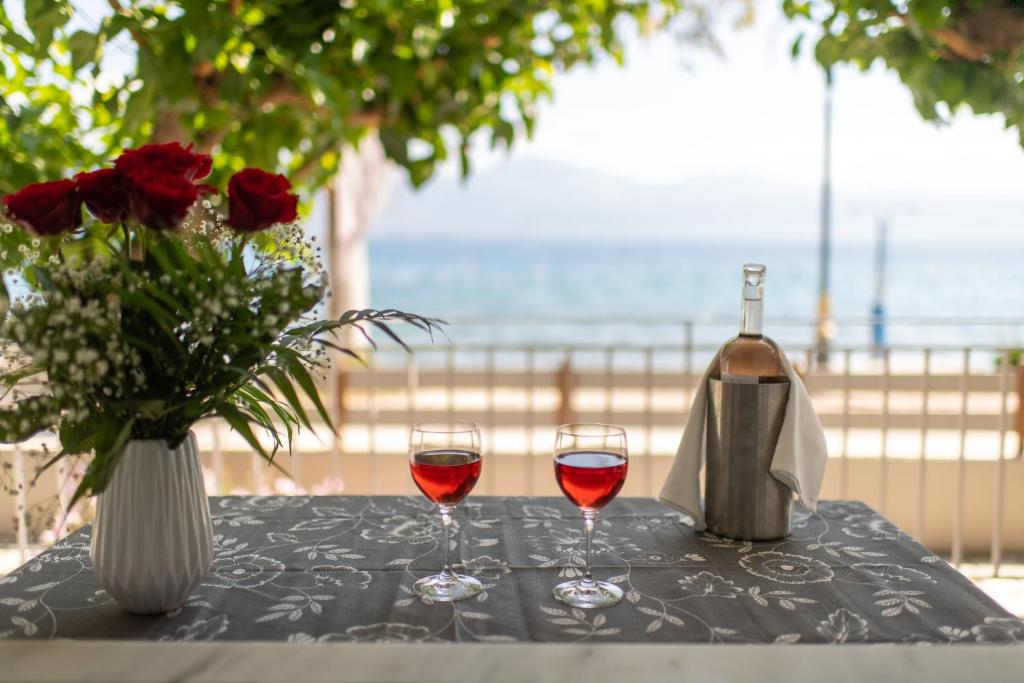 una mesa con dos copas de vino y un jarrón de rosas en Moukas Seaside Apartments Romantico, en Selianitika