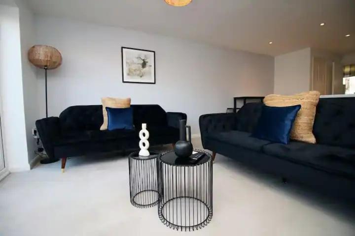 una sala de estar con 2 sofás negros y una mesa. en Seymour Way Stunning 4 bed with FREE parking, en Magor