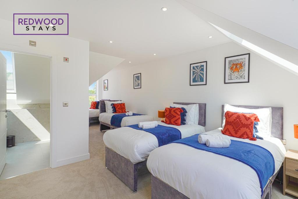 Habitación con 3 camas con almohadas azules y naranjas. en BRAND NEW Spacious 4 Bedroom Houses For Contractors & Families with FREE Parking, Garden, Fast Wifi and Netflix By REDWOOD STAYS, en Farnborough
