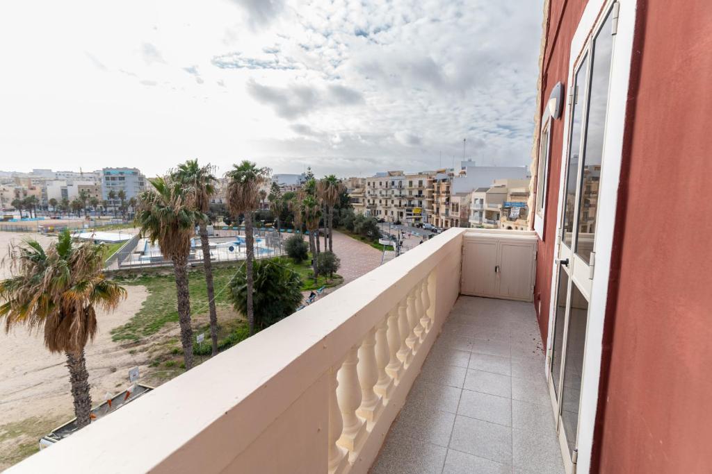 a balcony with a view of the beach and palm trees at Luxurious Beach Apartment in Birżebbuġa