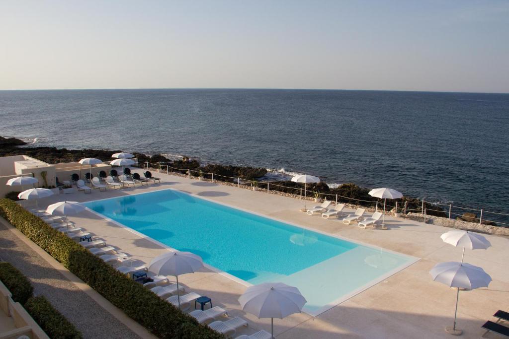 uma piscina com cadeiras e guarda-sóis junto ao oceano em Hotel La Sorgente em Savelletri di Fasano