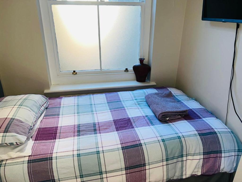 a bed with a plaid blanket and a window at Single Room - Bed for the night - Close to Beach in St. Leonards